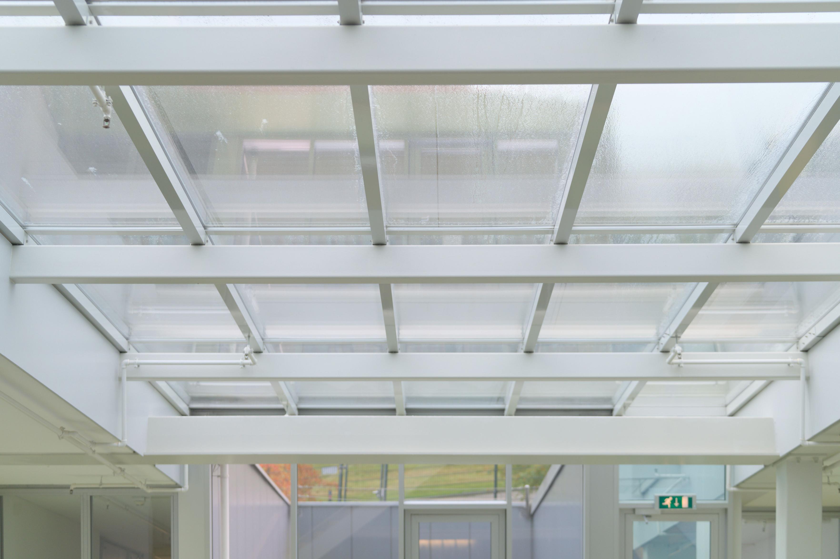 Rain on panes of glass suspended on grey painted metal beams spanning the ceiling.
