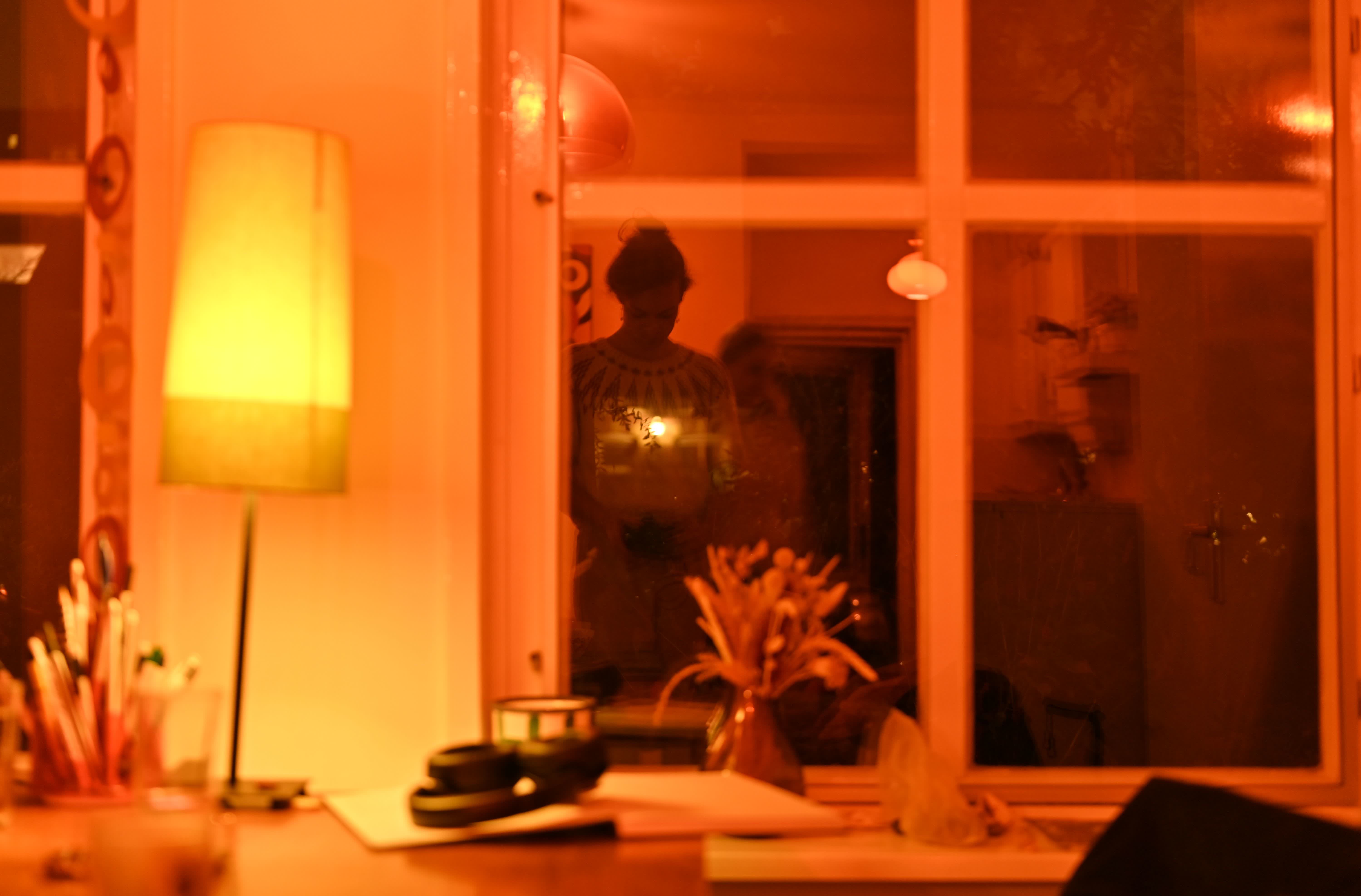 You can see me wearing a knit white wool sweater with a beautiful yoke in red yarn reflected in the window of a very warmly lit living room. My friend is walking just behind me and she is motion-blurred.